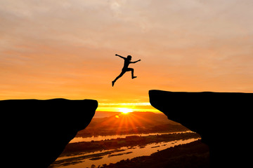 Courage man jumping over cliff on sunset background,Business concept idea - obrazy, fototapety, plakaty
