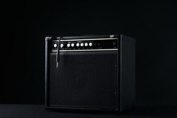 Black guitar amplifier with jack cable on black background. - obrazy, fototapety, plakaty