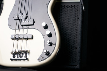 Black and white electric bass guitar with jack cable and classic amplifier on a dark...