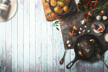 Overhead view of colorful roast vegetables, savory sauces and salt served with grilled t-bone steak on a rustic wooden counter in a country steakhouse created digital illustration