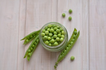 Top view of raw, sweet pea seeds in glass plate near green, split pea pods on wooden texture