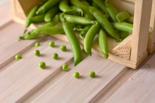 Scattered sweet, raw peas near wooden, brown box with full pea pods close up