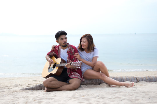 Cute hispanic couple playing guitar serenading on beach in love and embrace