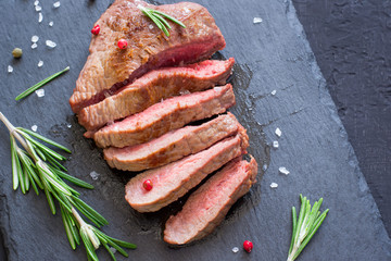 Roast beef steak with rosemary on slate cutting board. Grilled meat closeup