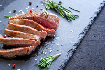 Roast beef steak with rosemary on slate cutting board. Grilled meat closeup