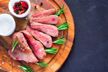 Roasted beef steak cut into slices with rosemary on wooden cutting board