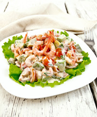 Salad with shrimp and tomatoes in white plate on board