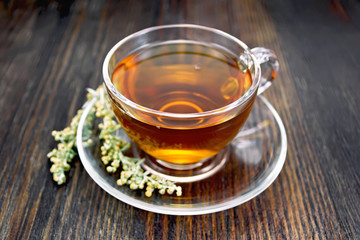 Tea with gray wormwood in glass cup on board