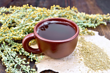 Obraz na płótnie Canvas Tea with wormwood in brown cup on board