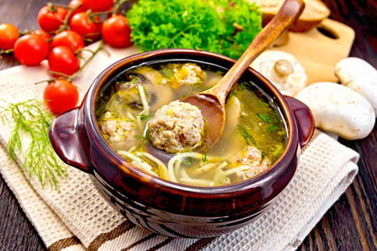 Soup with meatballs and spoon in clay bowl on board