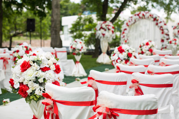 Wedding ceremony outdoors. White chairs with red ribbon.