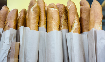 Fresh baked rustic bread loaves in paper bags on wooden shop shelf
