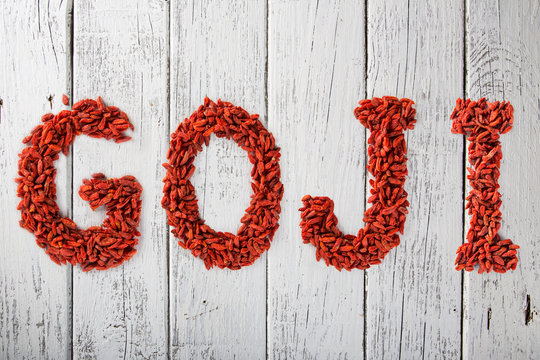 Goji berries as letters on old white wooden table.