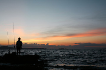 Fishing man silhouette on the stone at seaside AUG, 2016
