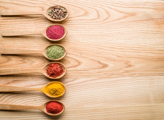 Assortment of colorful spices in the wooden spoons on the wooden table.