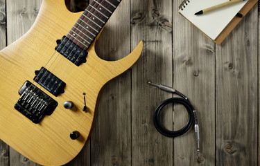 Fototapeta premium Chitarra Elettrica, Libretto per gli Appunti e Cavo Audio su Superficie di Legno Scuro Effetto Vintage