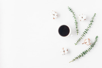 Workspace with cup of coffee, cotton flowers, eucalyptus branches. Flat lay, top view