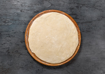 Pizza dough on a round board on dark stone surface
