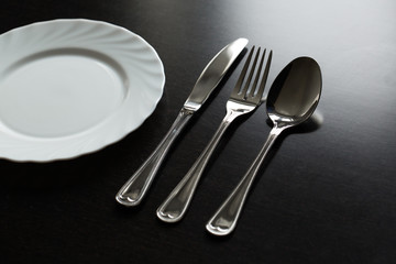 Cutlery on a black background. Fork, spoon, knife, plate.