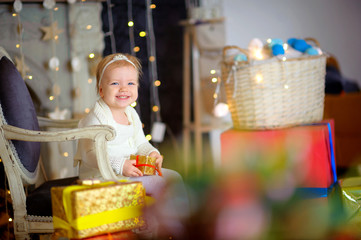 beautiful girl sits on a chair in an interior of studio with a gift box in hands, cheerfully smiles