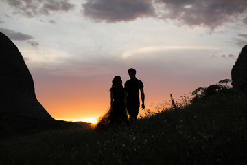 Fototapeta na wymiar Silhouettes of a young couple lovers at sunset in rays of setting sun