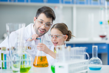 Man teacher and girl student scientists in protective glasses making experiment in lab