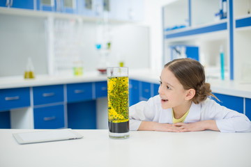 portrait of excited girl scientist looking at experimental tube in lab