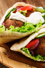 Falafel and fresh vegetables in pita bread on wooden table