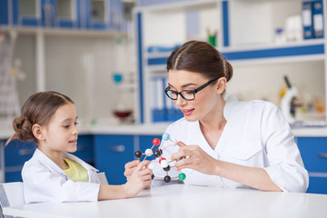 Smiling woman and little girl in lab coats working with molecular model