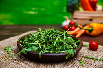 Arugula leaves in bowl. Fresh salad. Carrot, pepper and cherry tomatoes. Natural raw vegetables. Organic bio food on rustic wooden table.