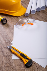 Fototapeta premium Protective glasses and helmet. Flashlight, knife and architecture plans. Blank sheet of paper. Wooden rustic background.