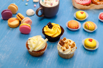 Cupcakes, macaroons and donuts. Mug with whipped cream and marshmallows. Almond macaron cookies. Sweet dessert.