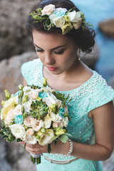 Bride in nature in the mountains near the water. Dress color Tiffany. Bride posing with bouquet.