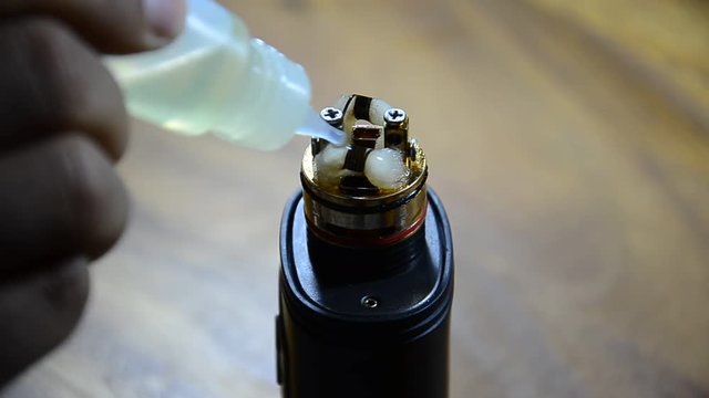 Man filling an electronic cigarette with e-juice. Man detaching the reservoir tank from the atomizer and battery to fill it with flavored liquid (e-juice) that may or may not contain nicotine.