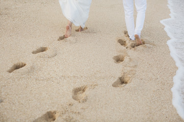 Fototapeta na wymiar The bride and groom walk hand in the sand. footprints in the sand near the ocean