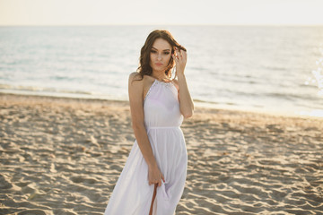 Fototapeta na wymiar Beautiful girl bride in a white dress and sneakers, at sunset walks along the beach.