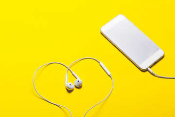Close-up of smart phone with headphones on a yellow background. (Top view). Listen to music.
