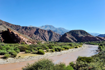 River at coloured rock mountains. Hill of Seven Colors over Purmamarca village. Quebrada de Humahuaca valley, a UNESCO World Heritage Site, Argentina.