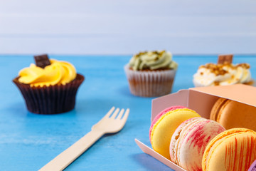 Macaroon cakes. Cupcakes with pistachio nuts cream and Almond macaron cookies. Delivery box. On blue wooden rustic background.