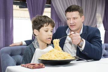 Dad feeding his son spaghetti in a restaurant 