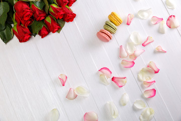 Macaroon cakes with bouquet of red roses. Different types of macaron. Colorful almond cookies. White wooden rustic background.