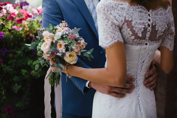 Wedding. The groom in a suit and the bride in a white dress standing side by side and is holding bouquet of white flowers and greenery