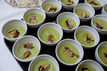 Crema verde con cozze e pancetta dentro ciotole bianche 