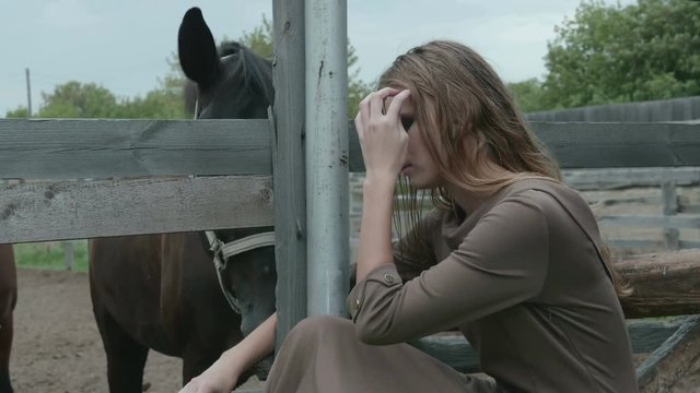 Beautiful girl sitting next to a horse paddock