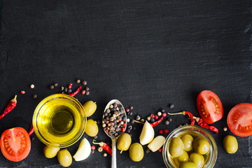 Top view of olive oil and ingredients for a healthy vegetarian salad - cherry tomatoes, olives, garlic and rosemary on natural black slate background with copy space for your text