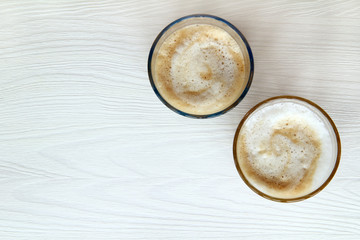 coffee for two/ Glass glasses with frothy cappuccino on the background of a light wooden table top view