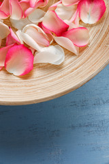Petals of white and pink roses on blue painted rustic background. Fresh natural flowers in bowl. Dirty grunge wooden board.