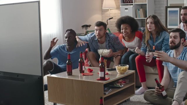 Interracial group of young excited sport fans watching match on TV at home. They covering face with hands and getting sad after failure of their team
