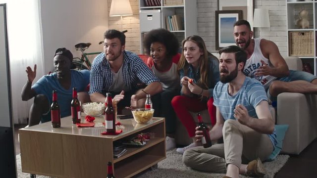 Zoom in of multi-ethnic group of friends celebrating victory of their team. They yelling, clapping hands and whistling while sitting in living room and watching TV match 