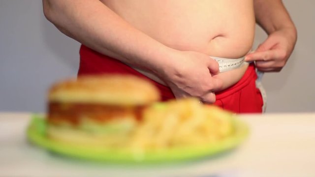 Overweight woman measure girth of her belly, against hamburger. Fast food. obesity